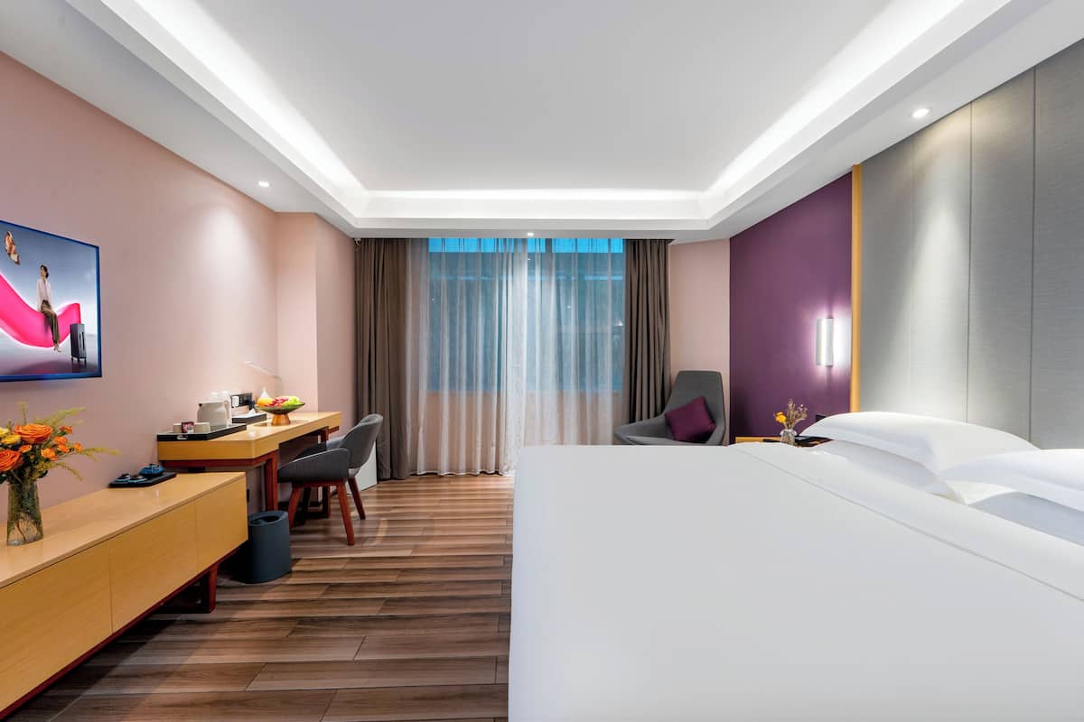 Una camera d'albergo moderna con un letto, una scrivania, una sedia e un'ampia finestra con tende.