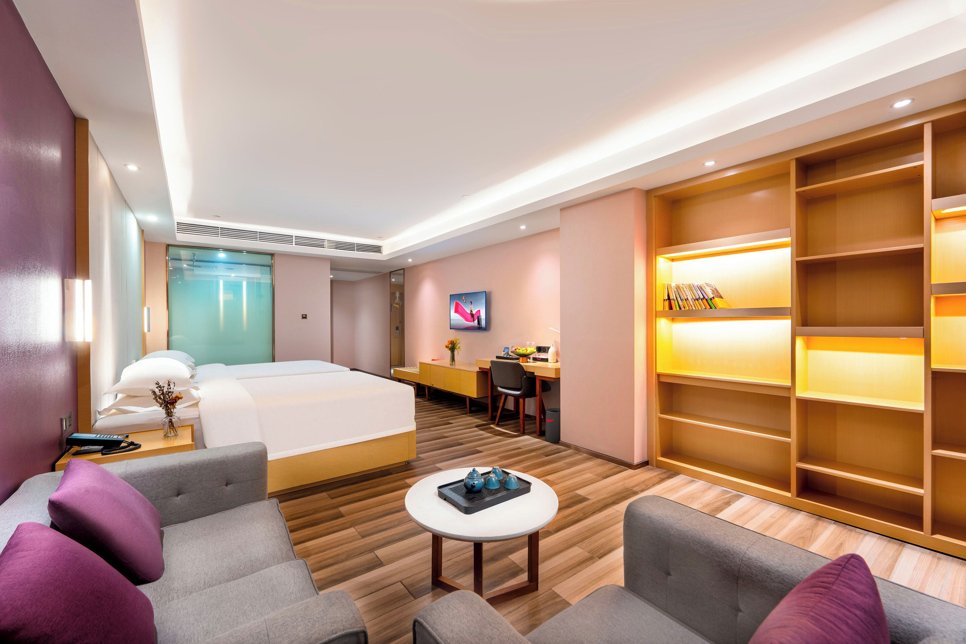 A modern hotel room with a bed, a desk, a TV, and a seating area with a coffee table.