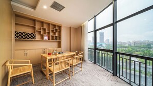 A modern room with a large window, a wooden dining table with chairs, and built-in shelving. - Trendy Romantic MAXScreen Hotel (Guangzhou)
