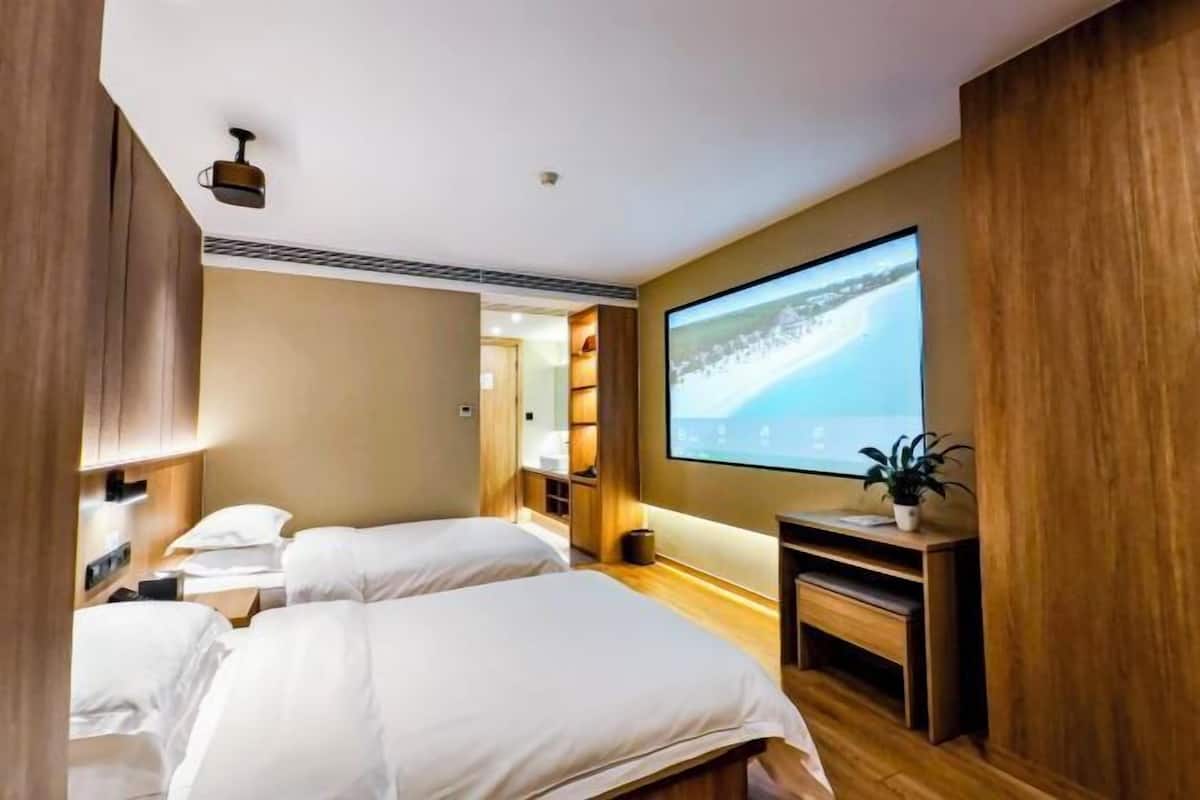 Habitación de hotel con dos camas, una pantalla de televisión, una mesita con una planta y paneles de madera.