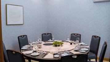 Une salle de conférence avec une table ronde disposée pour huit personnes, entourée de chaises, un tableau encadré au mur et un appareil de climatisation au-dessus.