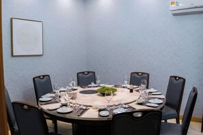 A conference room with a round table set for eight, surrounded by chairs, with a framed picture on the wall and an air conditioning unit above. - Shanghai Lu'an Hotel (Ningguo Road) (Shanghai)