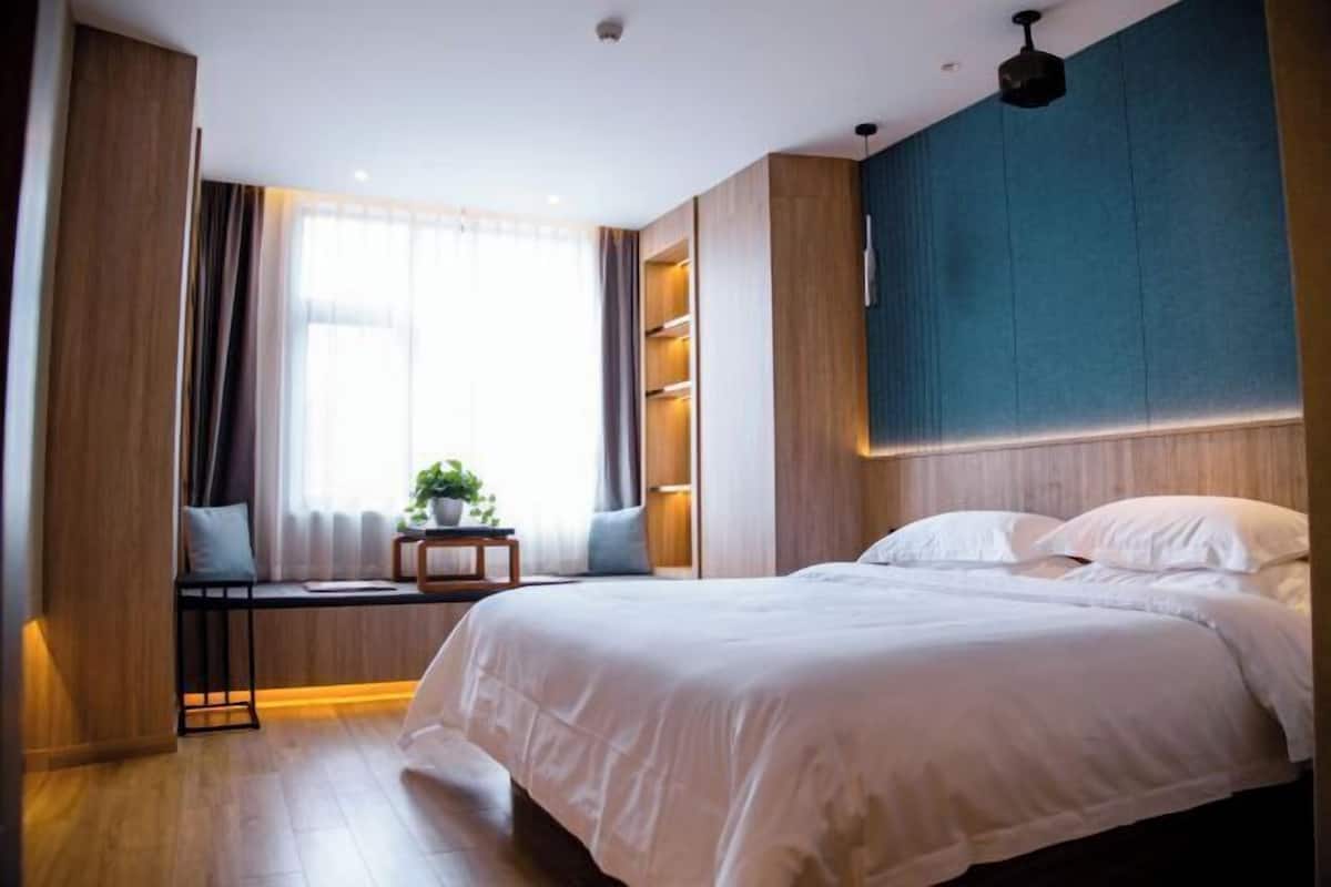Un dormitorio moderno con una cama grande, estanterías empotradas, un ventanal con cortinas y una mesita con una planta.