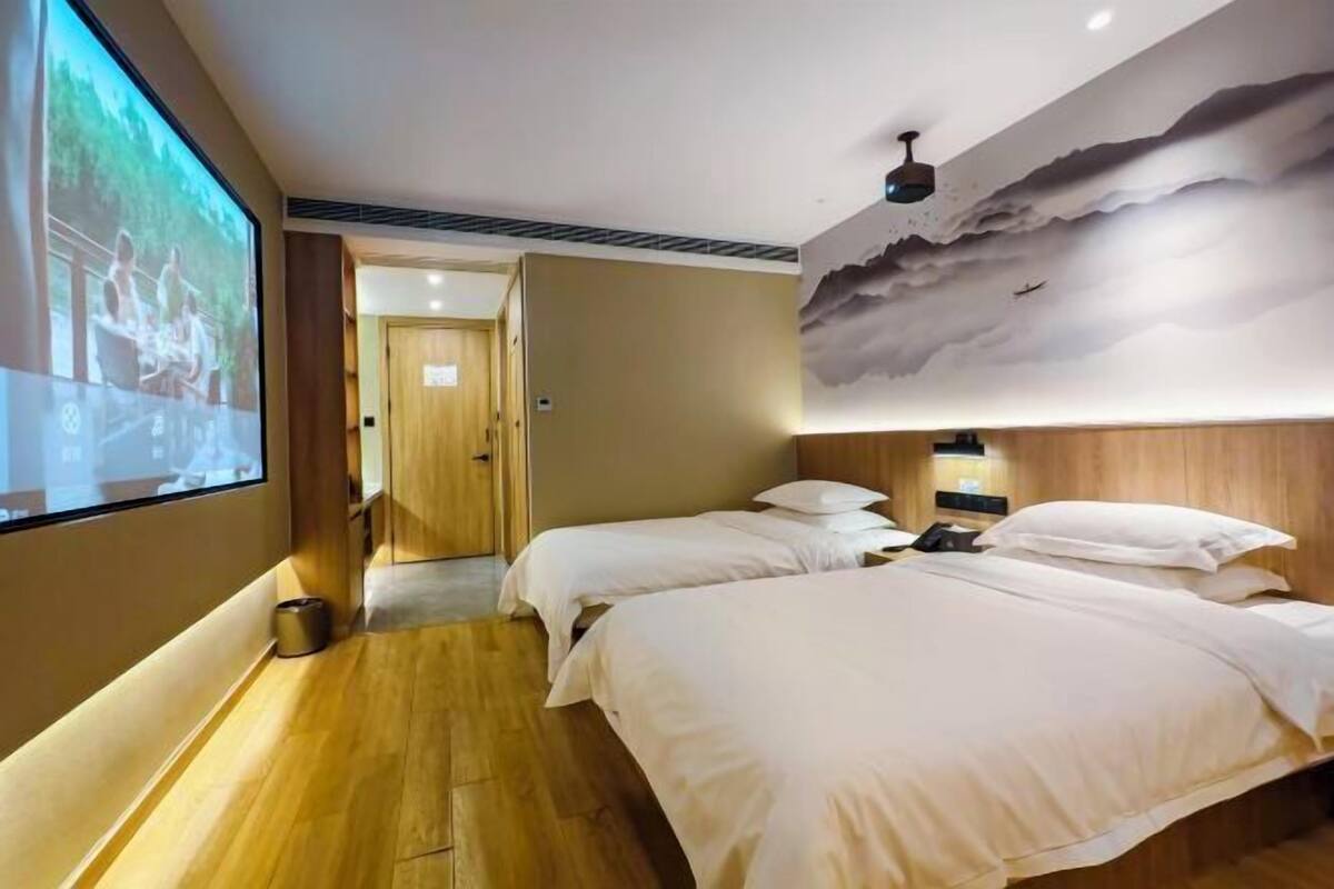 Habitación de hotel con dos camas, una pantalla grande, suelo de madera y un mural único en el techo.