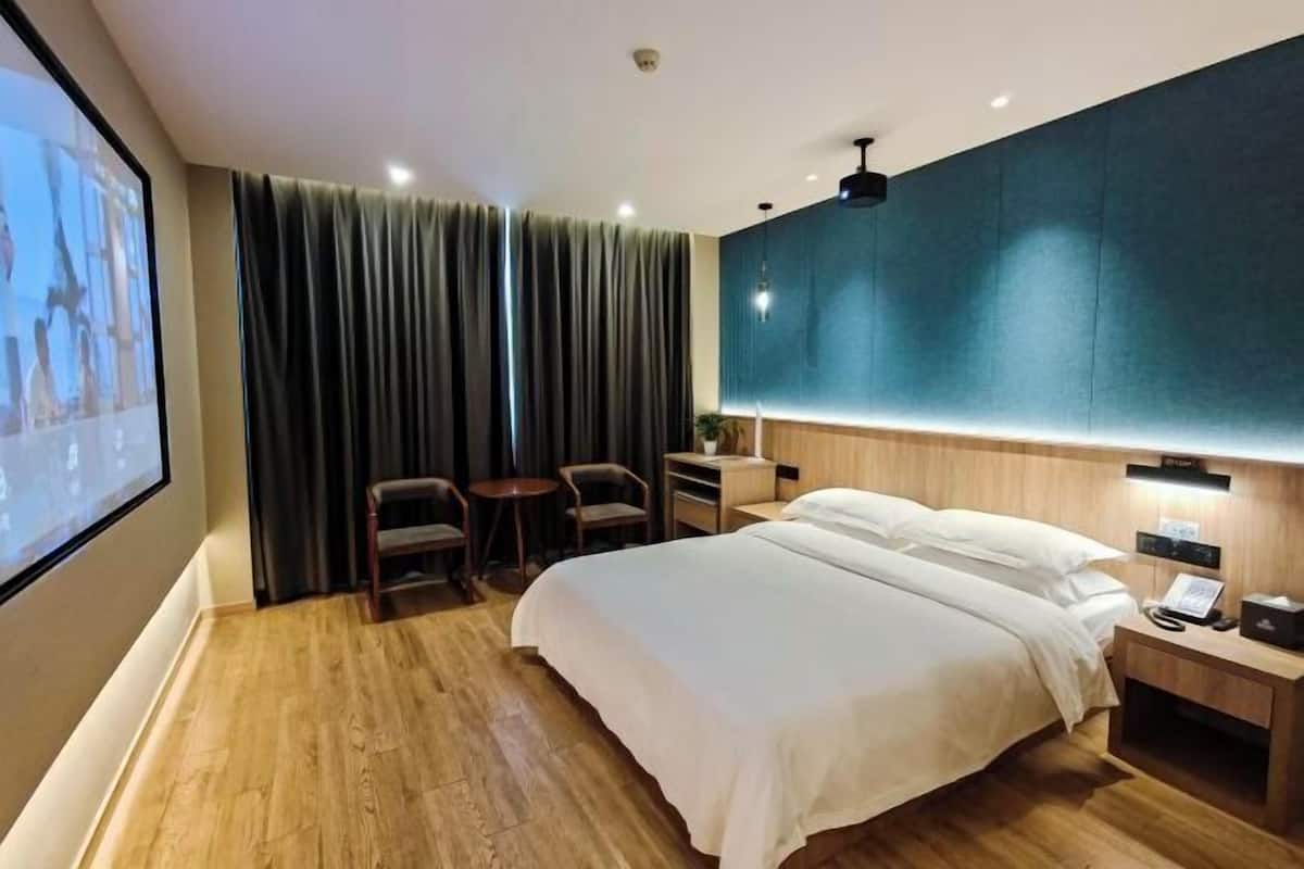 Una habitación de hotel con cama, escritorio, silla, televisor y un amplio ventanal con cortinas.