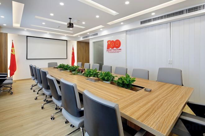 Un salón de conferencias con una larga mesa, sillas, una pantalla de proyector y un logotipo en la pared.