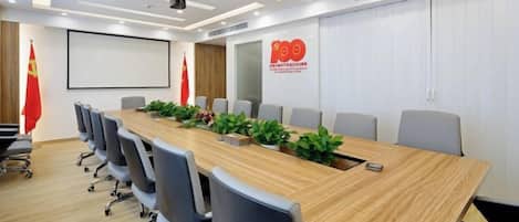 Un salón de conferencias con una larga mesa, sillas, una pantalla de proyector y un logotipo en la pared.