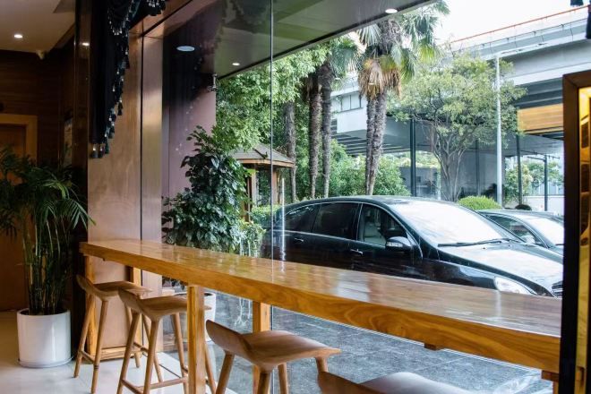 A bar area with a wooden counter and stools, a large window with a view of parked cars and greenery outside.