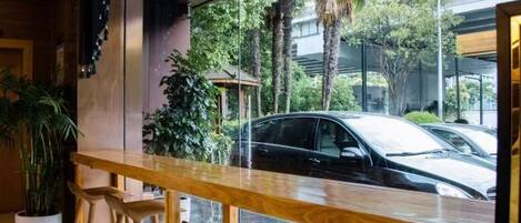 A bar area with a wooden counter and stools, a large window with a view of parked cars and greenery outside.