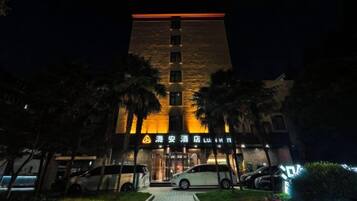 Um edifício com entrada destacada, área de estacionamento e fachada bem iluminada à noite.