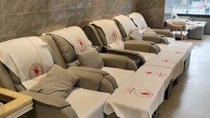 Una fila de sillones de masaje con reposapiés, cada uno cubierto con un mantel blanco y un logotipo.
