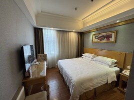 Una habitación de hotel con cama, escritorio, silla, televisión, un cuadro en la pared y una ventana con cortinas.