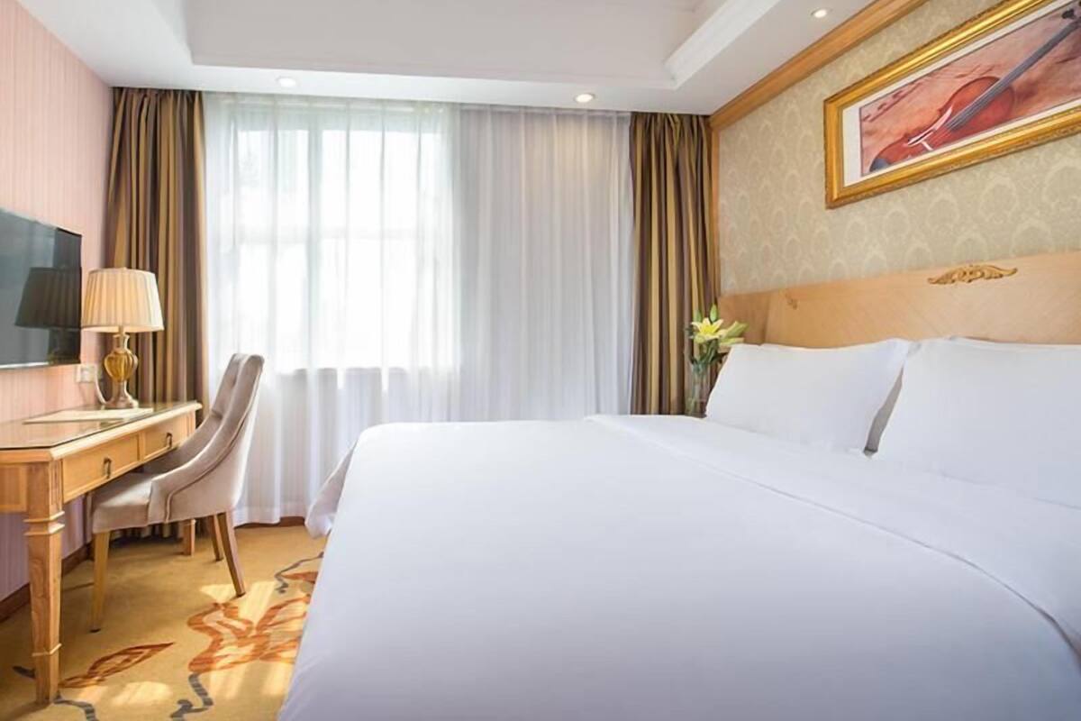 A hotel room with a large bed, a desk with a lamp, a chair, and a television.