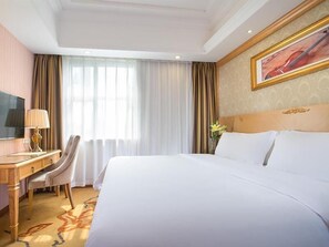 A hotel room with a large bed, a desk with a lamp, a chair, and a television. - Vienna 3 Best Hotel Guangzhou Canton (Guangzhou)
