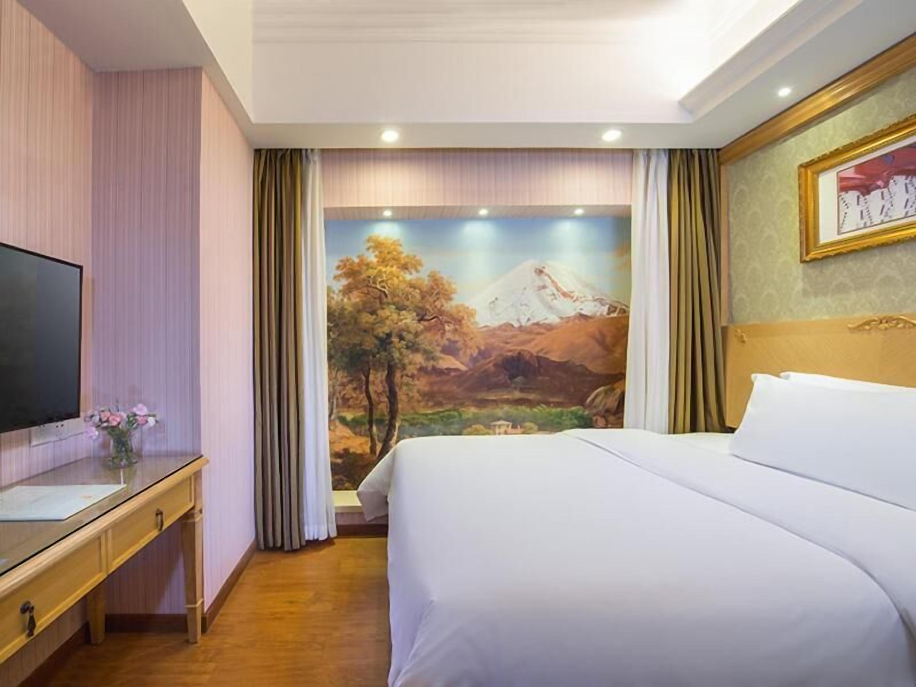 Ein Hotelzimmer mit Bett, Schreibtisch, Fernseher und einer Wandmalerei von einer Berglandschaft.
