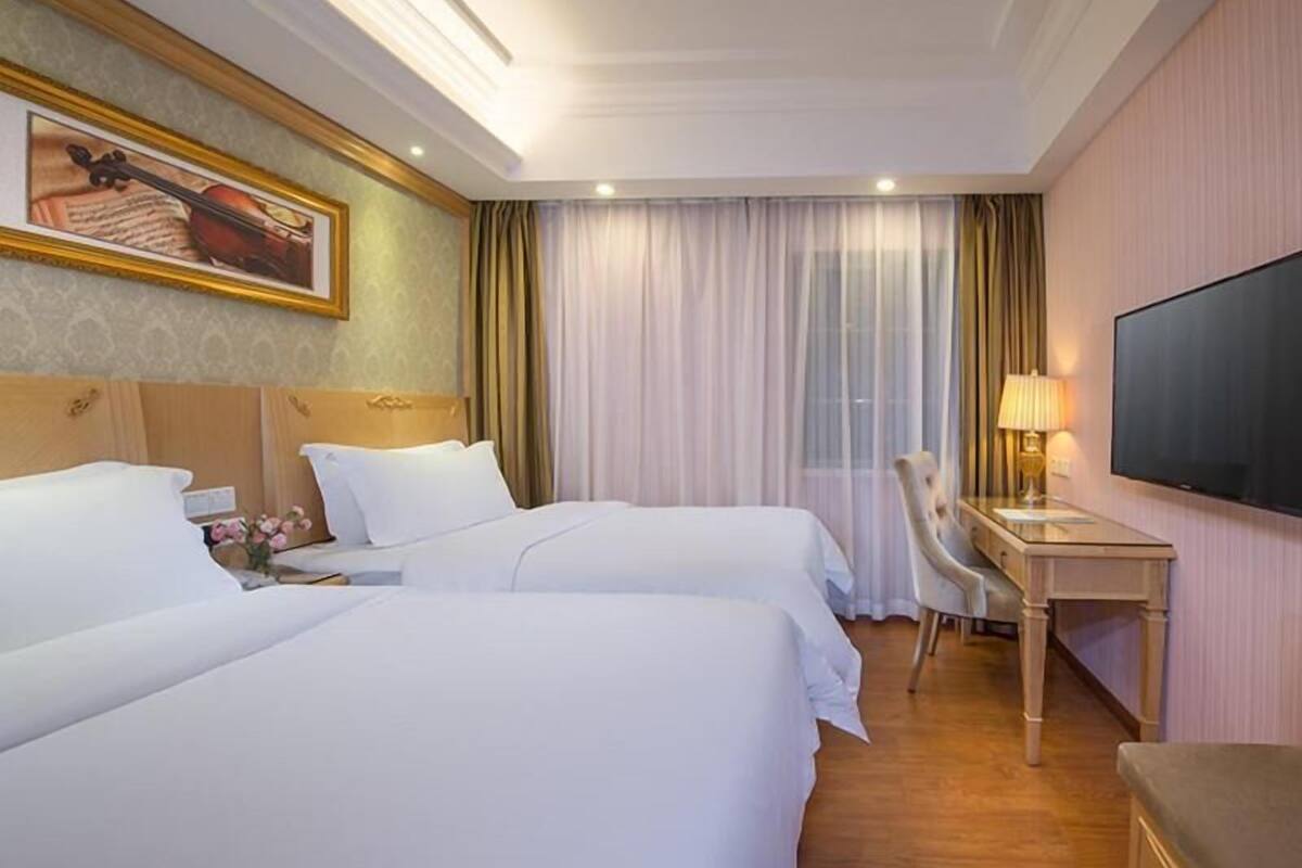 A hotel room with two beds, a desk, a chair, a television, and a window with curtains.