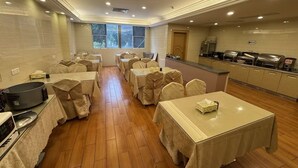 Un comedor con mesas y sillas, un área de cocina con estaciones de buffet y una ventana que proporciona luz natural.