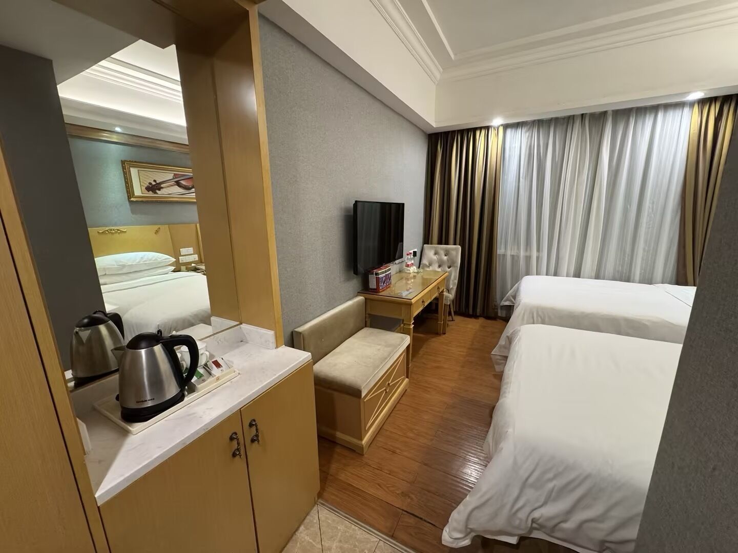 Een hotelkamer met een bed, een bureau met televisie, een minibar en een spiegel.
