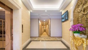 Un pasillo de hotel con piso de mármol, un espejo con marco dorado y un televisor montado en la pared.
