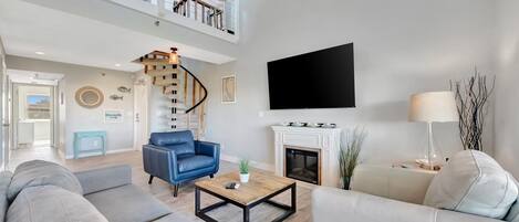 Een ruime woonkamer met een hoge nok, een trap, een flatscreen-tv, een open haard en een plafondventilator.