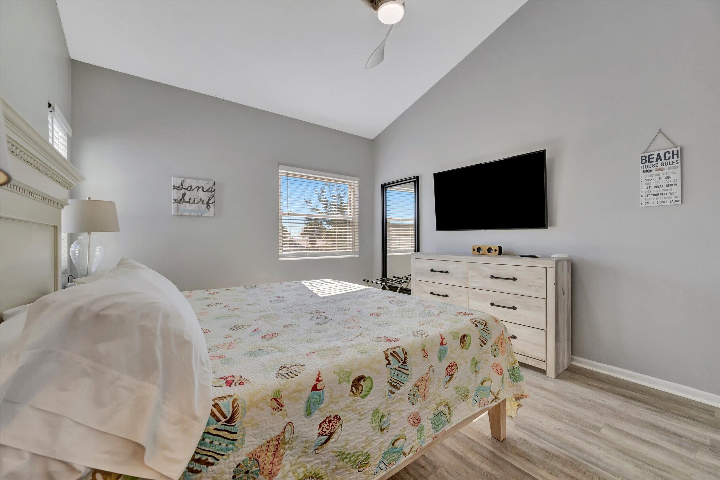 Un dormitorio con cama, televisor, cómoda y ventana con persianas.
