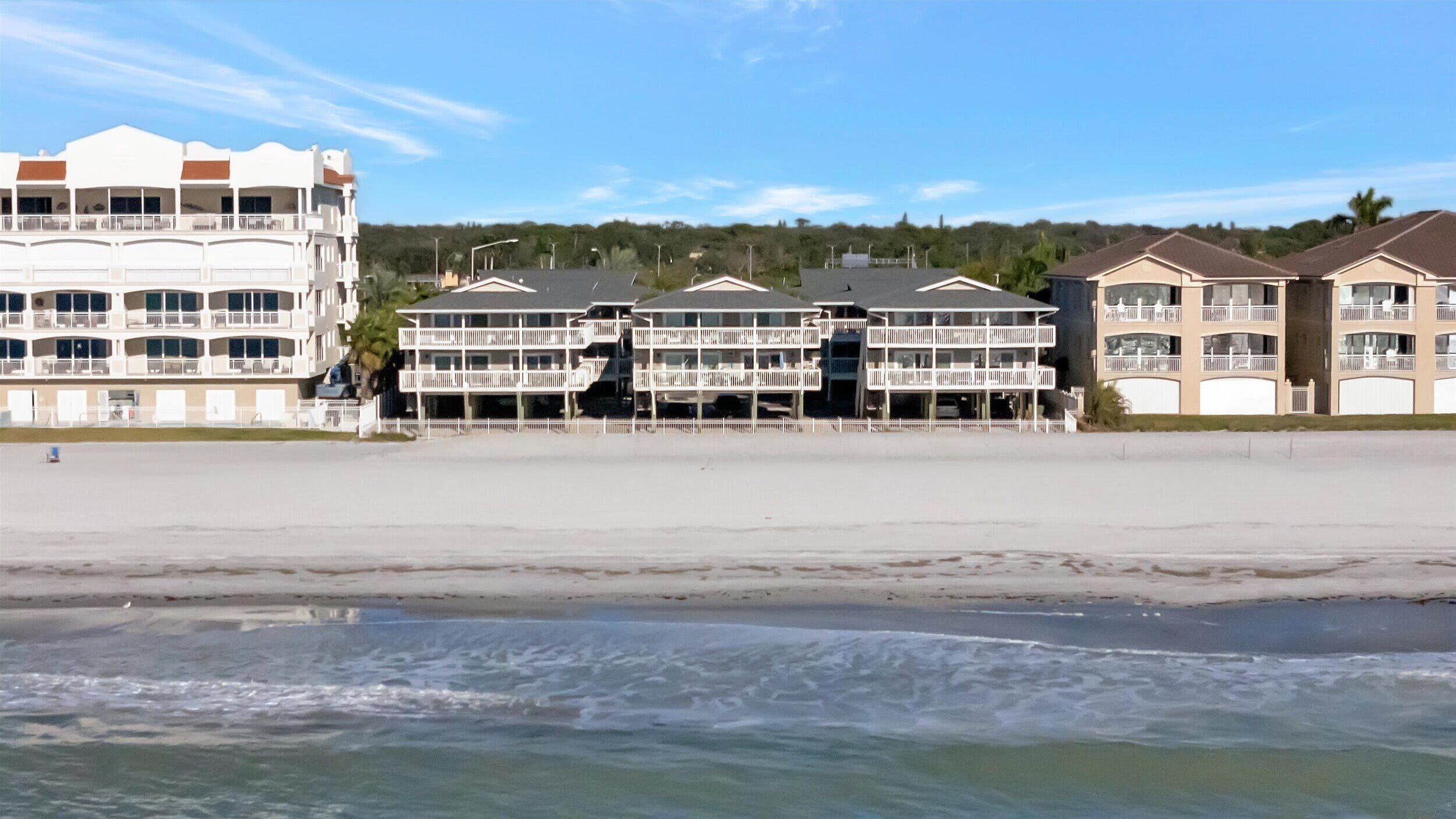 A beachfront hotel with multiple balconies and a sandy beach in the foreground.