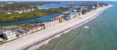 Vista aérea de una ciudad costera con una extensa playa, una zona urbana densa y un río que corre paralelo a la playa.