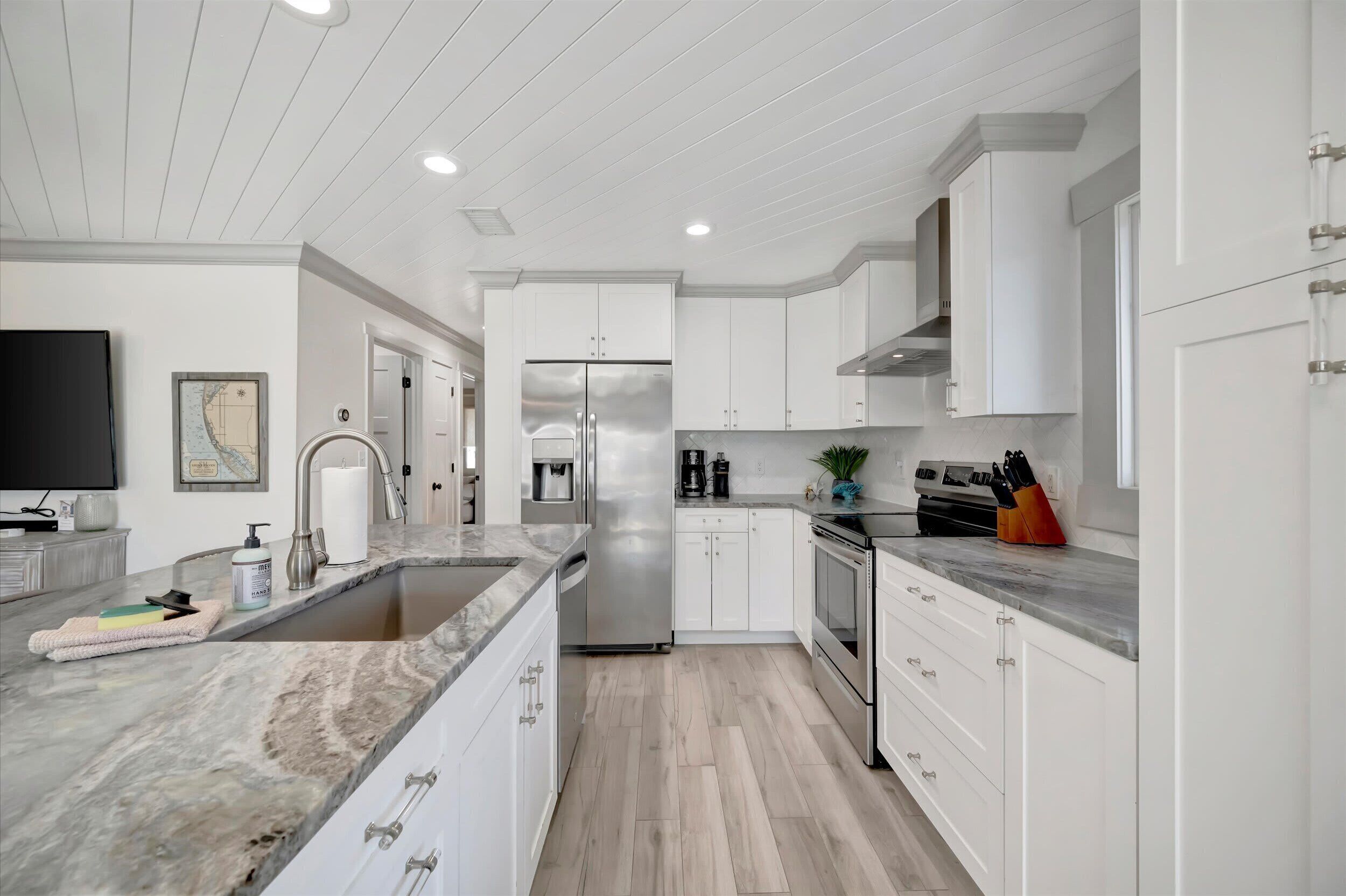 A modern kitchen with white cabinetry, stainless steel appliances, and a marble countertop.