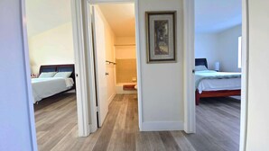 Hotellihuone, jossa on kaksi sänkyä, kylpyhuone, jossa on kylpyamme, ja käytävä, joka johtaa toiseen huoneeseen.