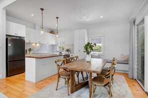 A modern kitchen with white cabinetry, a wooden dining table, and a built-in island. - Paddy's Place - 6 Paddy's Crt, Bangalow (Byron)