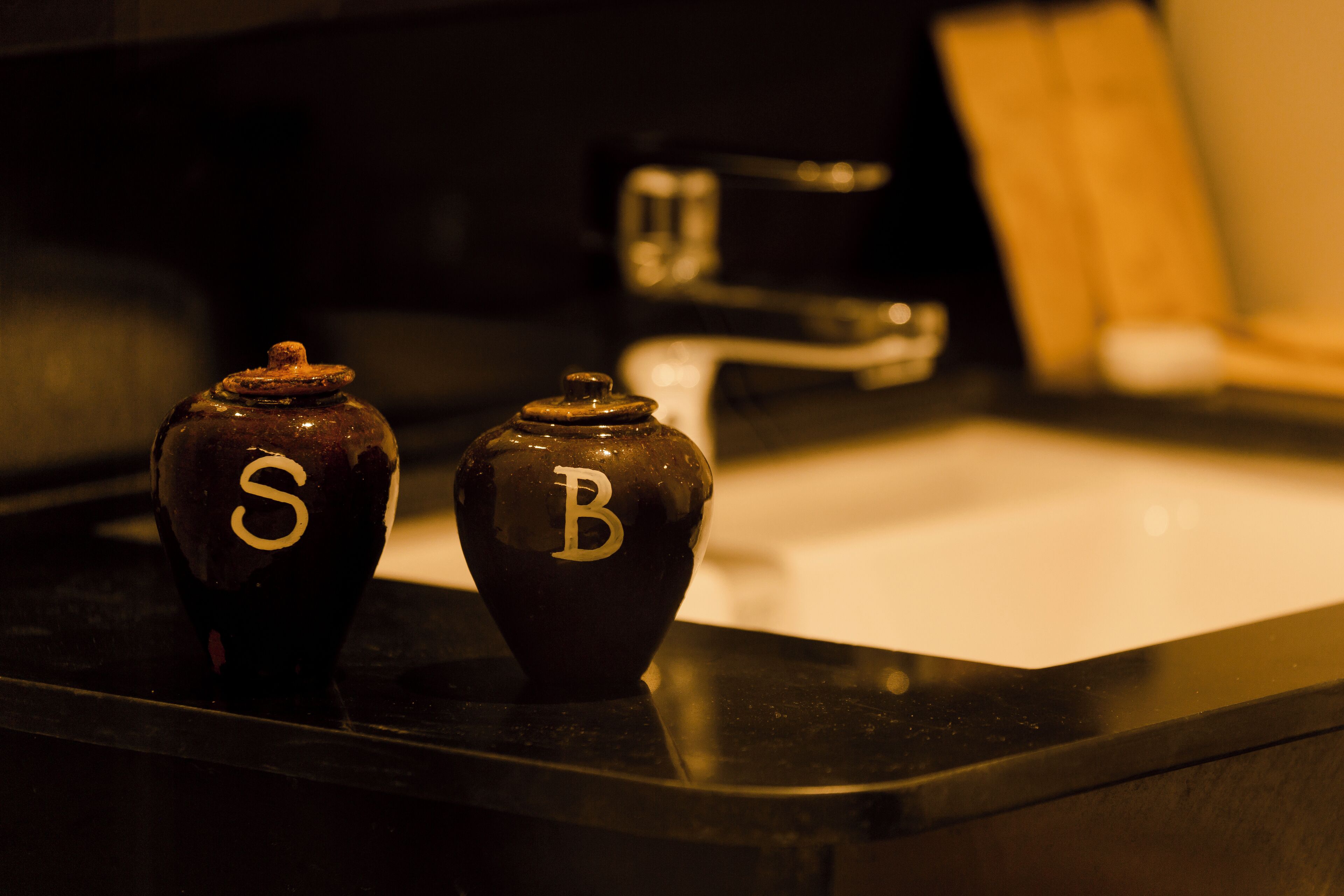 Two dark-colored ceramic containers with letters 'S' and 'B' on a kitchen counter.