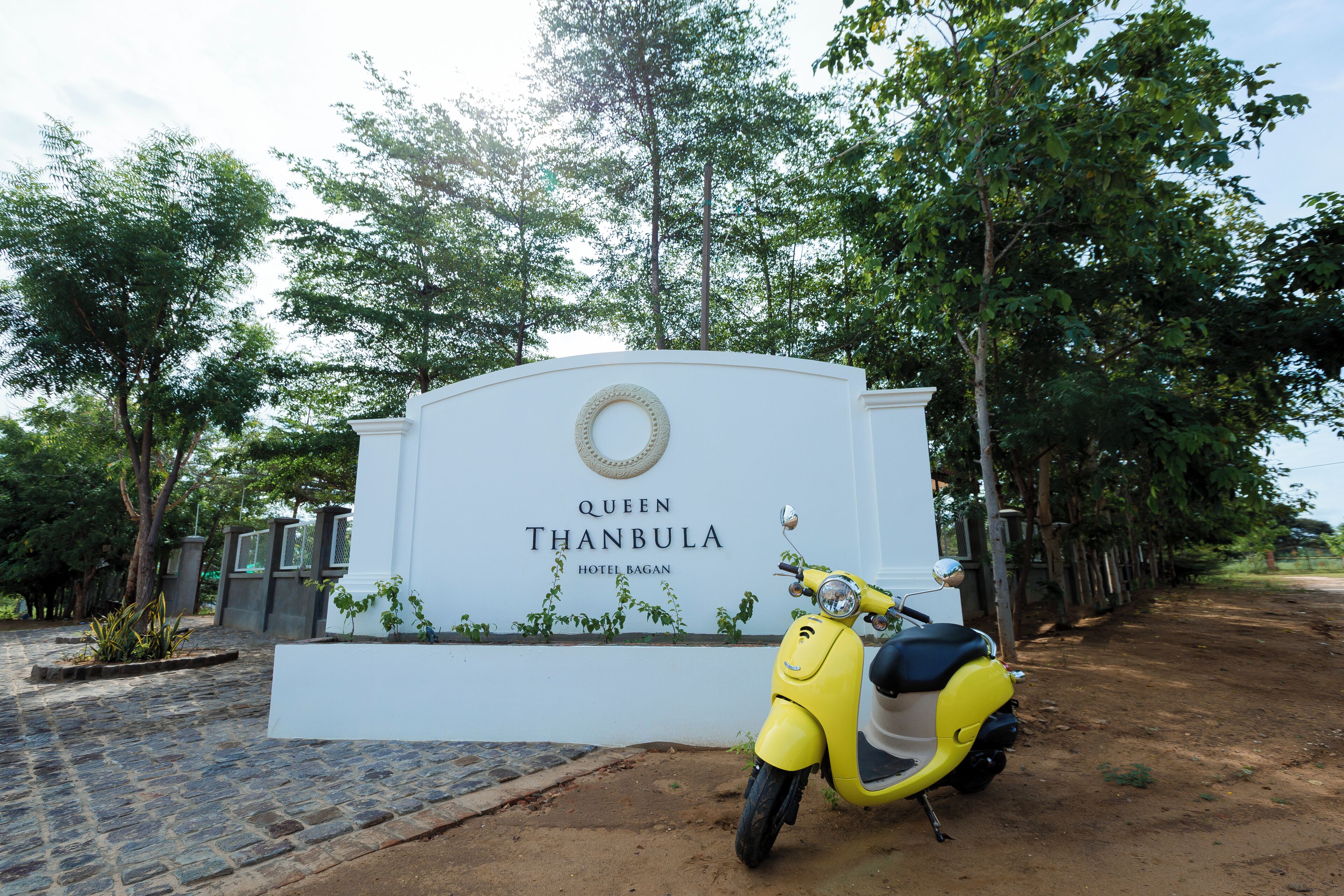 A yellow scooter parked in front of a sign for the Queen Thanbula Hotel Bagan.