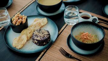 Una mesa de comedor con diversos platos, incluyendo un tazón de sopa, un plato con fideos y vegetales, y un postre.