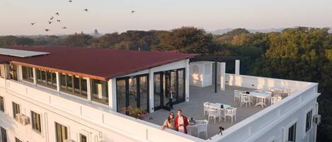 A rooftop terrace with outdoor seating, a view of the surrounding landscape, and a building with multiple windows.