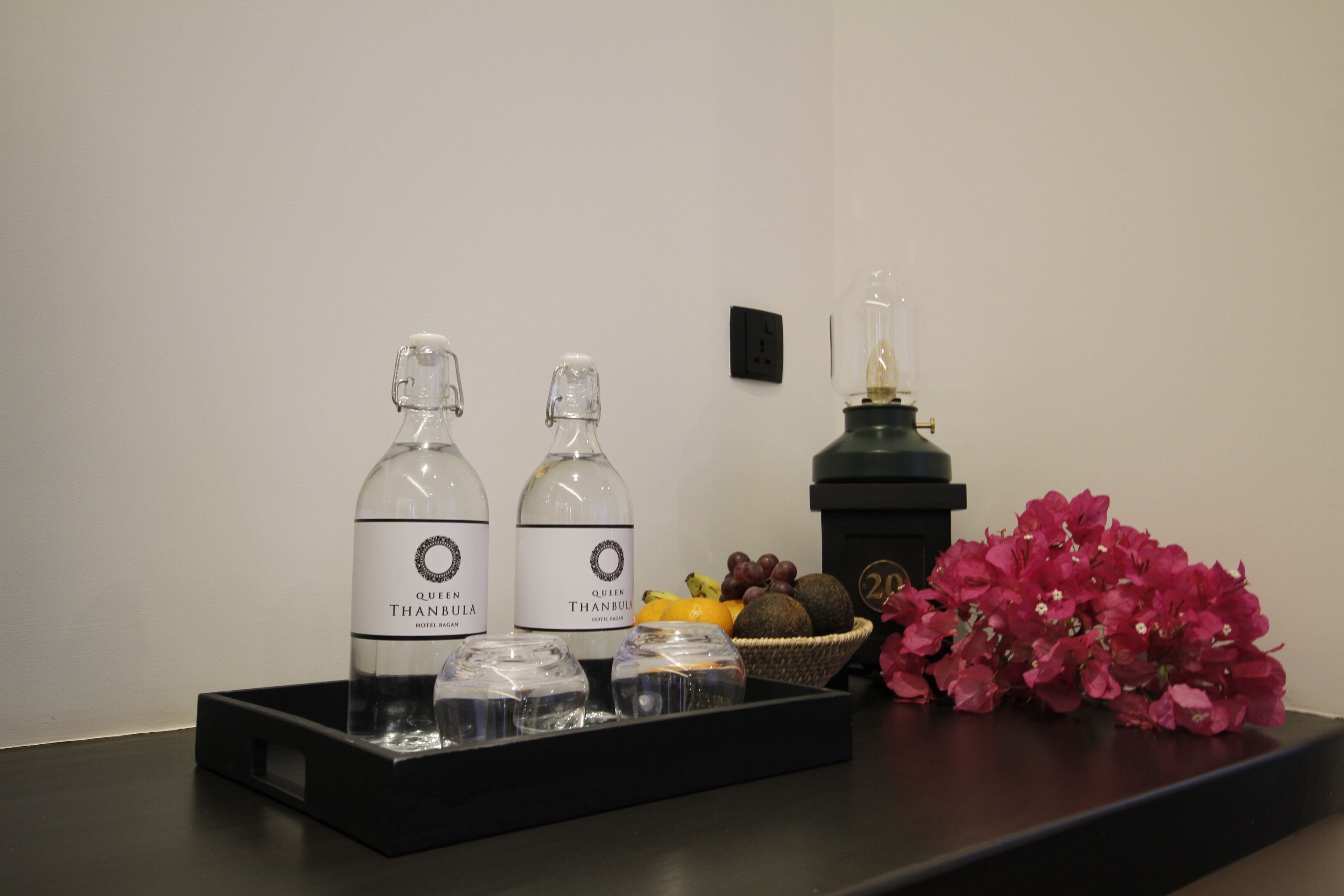 Due bottiglie del bar dell'hotel Queen Thanbula, una bottiglia di vetro e un cesto di frutta su un vassoio nero.