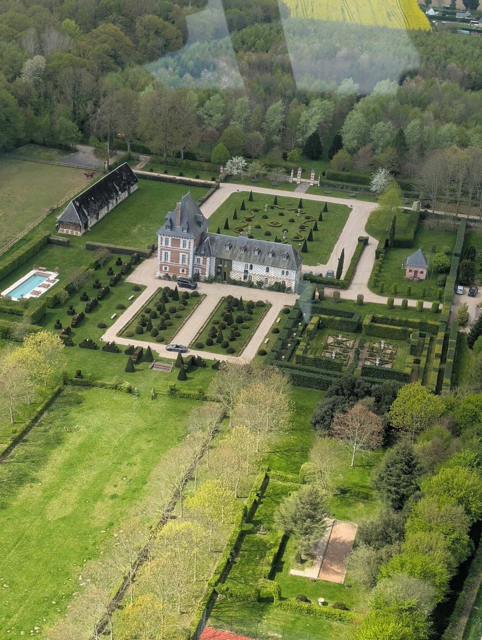 An aerial view of a large estate with a main building, extensive gardens, and a swimming pool.
