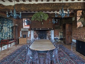 A dining room with a long wooden table, clear chairs, hanging chandeliers, a brick fireplace, and a large tapestry on the wall. - Private Norman Château for 12 - Near Deauville & Paris (Bouquetot)