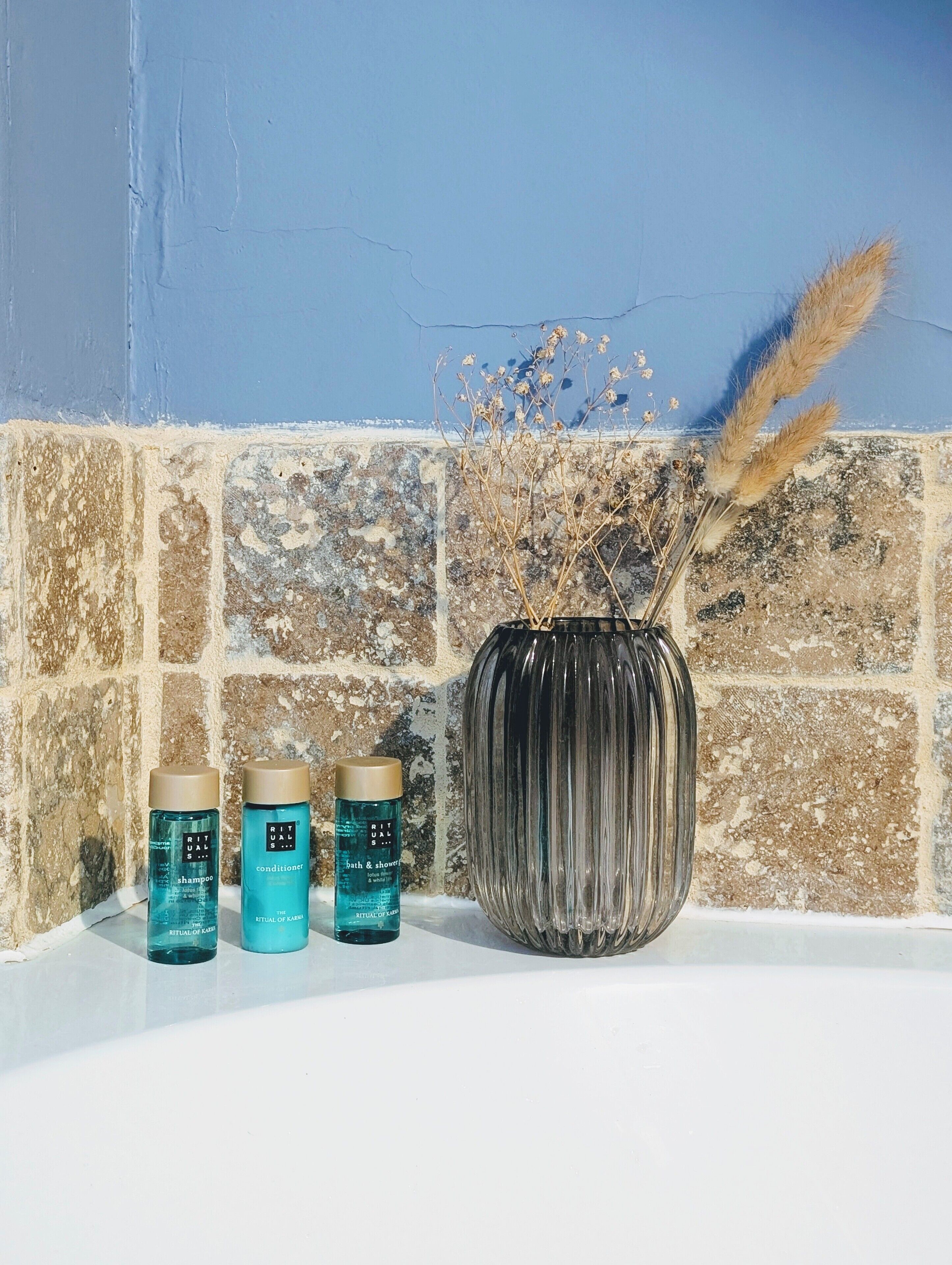 Ein Badezimmer mit gefliesten Wänden, einer großen Vase mit Trockenpflanzen und zwei Flaschen Haarpflegeprodukten.