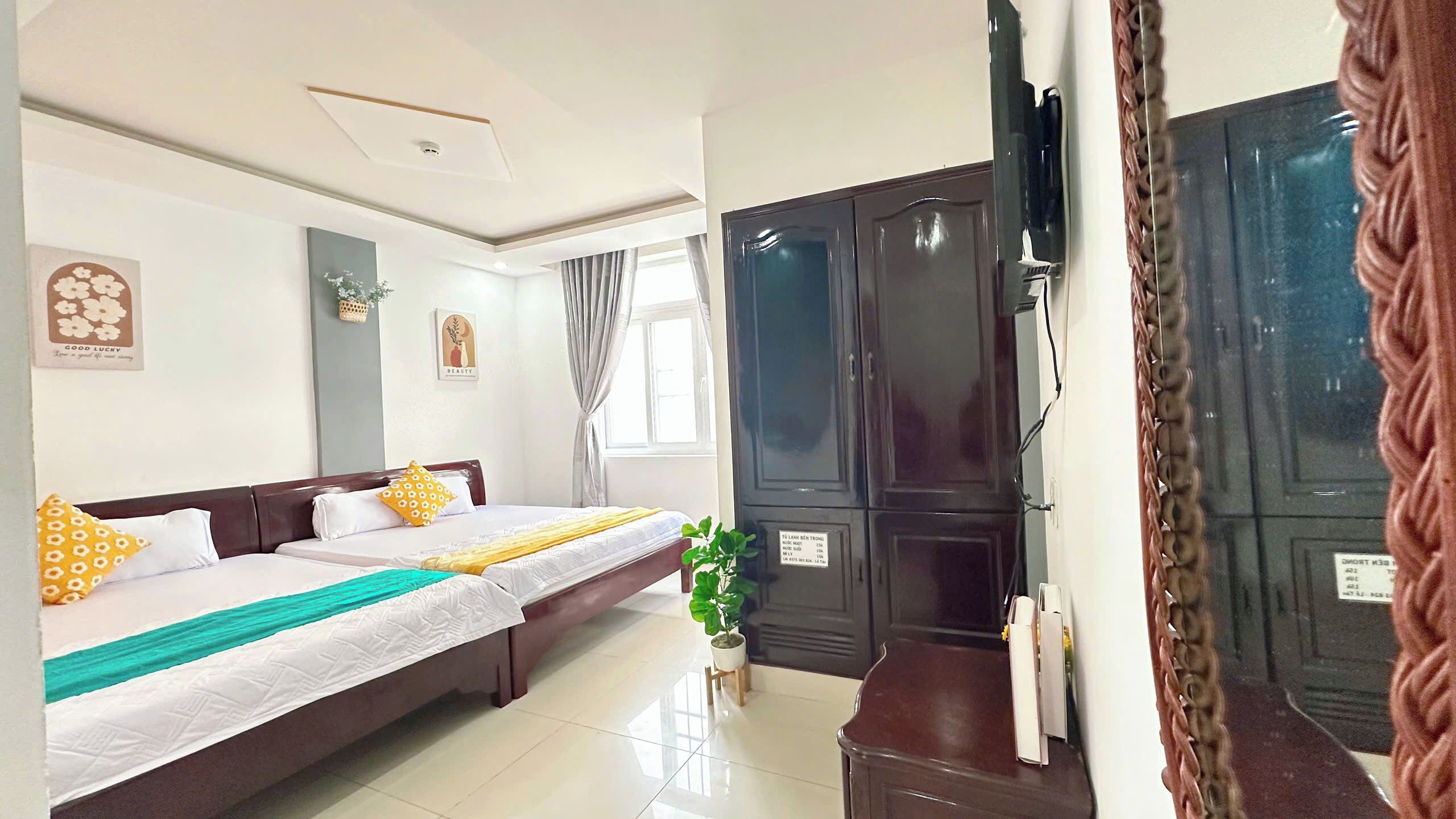 A hotel room with two beds, a large wardrobe, and a small potted plant.