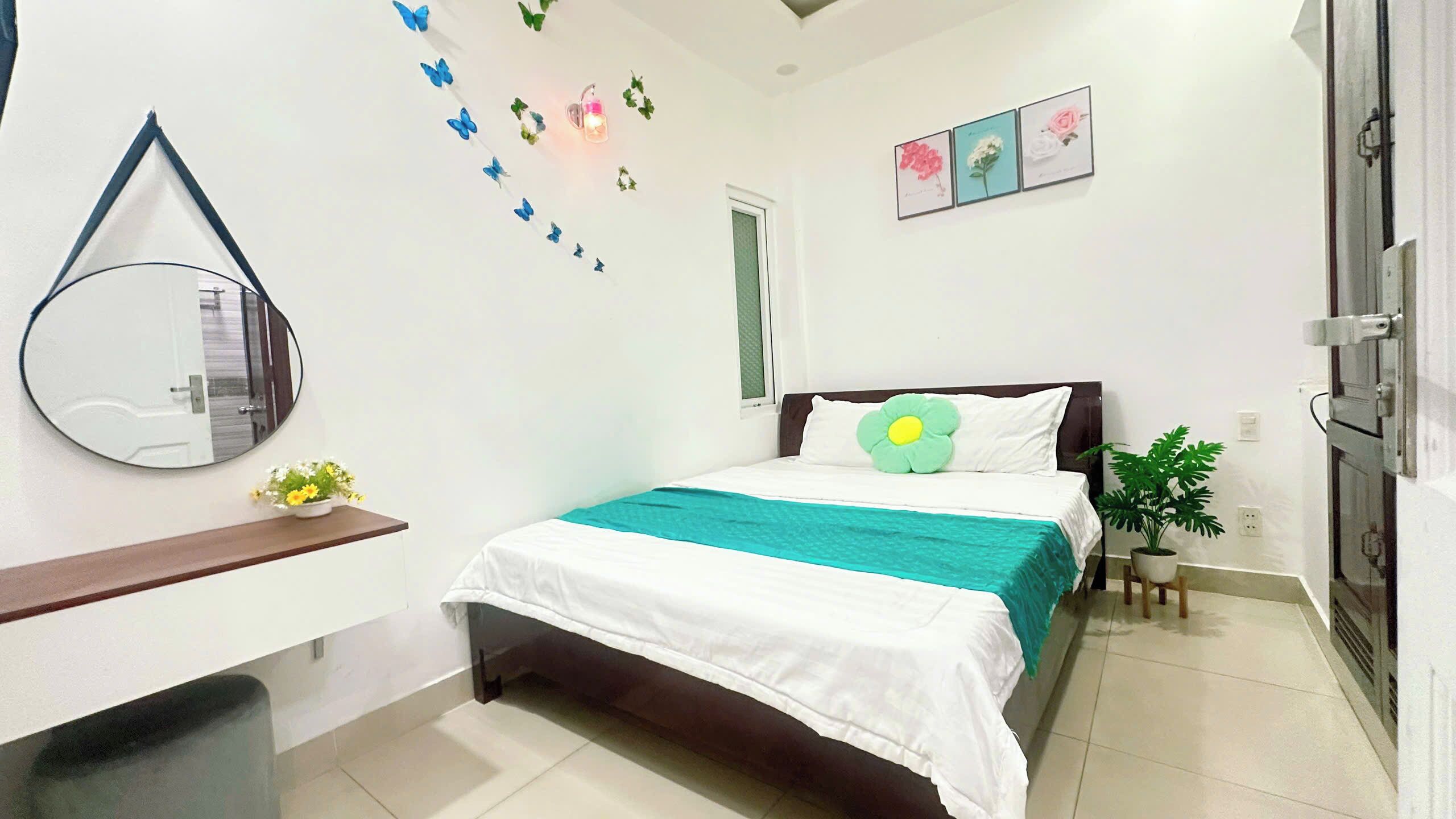 A bedroom with a bed, a bedside table, a mirror, a window, and wall decorations.