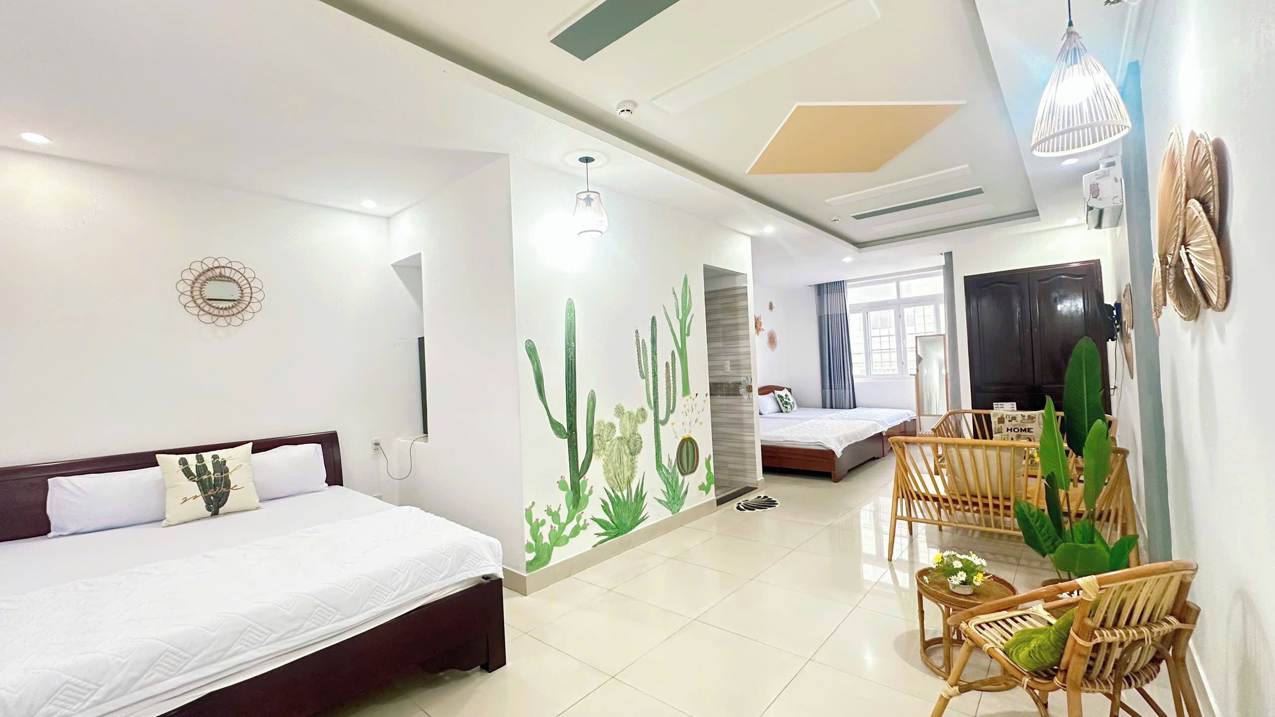A hotel room with a bed, a small seating area with chairs, a dining table, and a wall with a cactus mural.