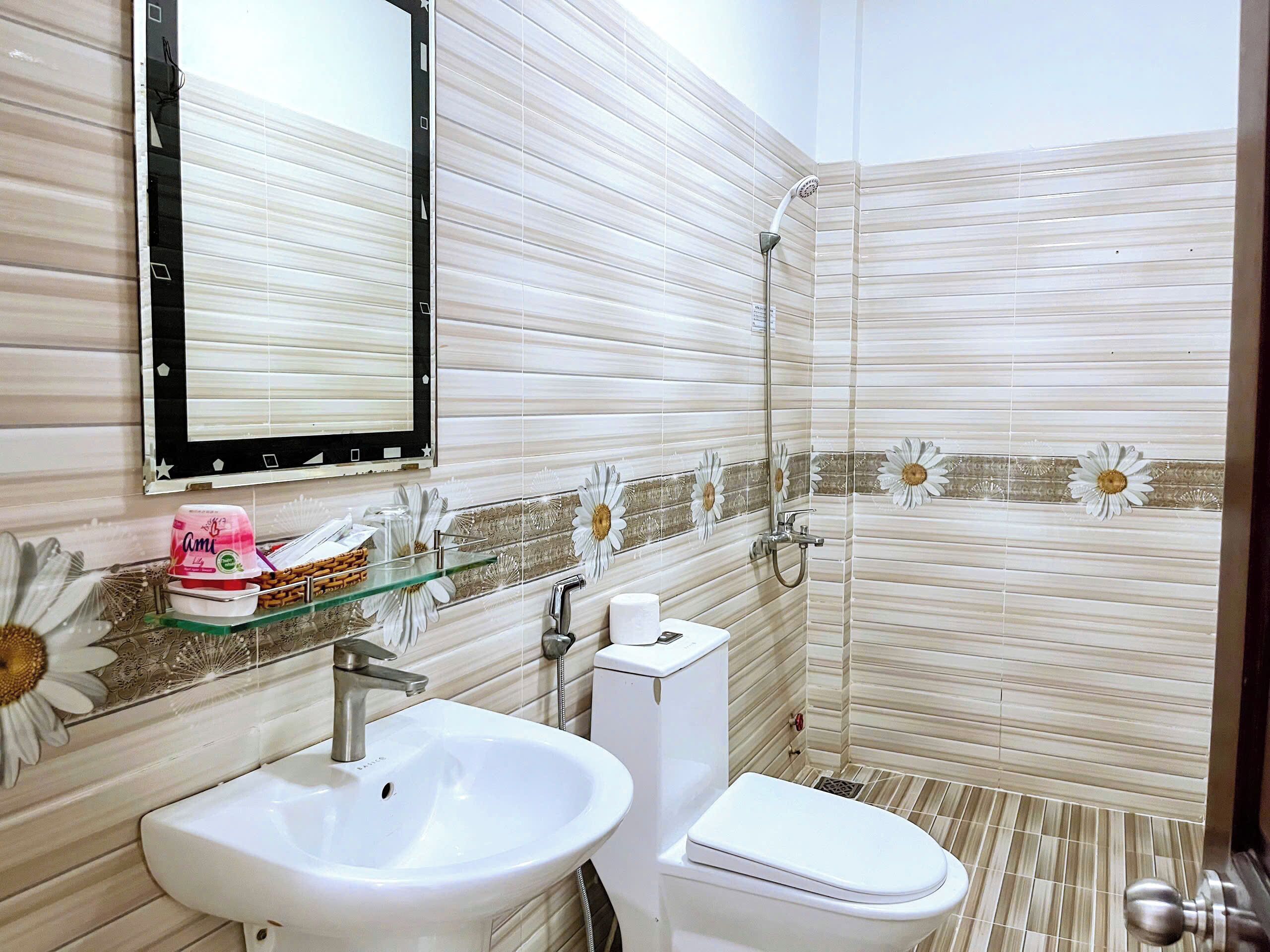 A bathroom with a white sink, toilet, and shower. There is a mirror above the sink and a decorative flower pattern on the walls.