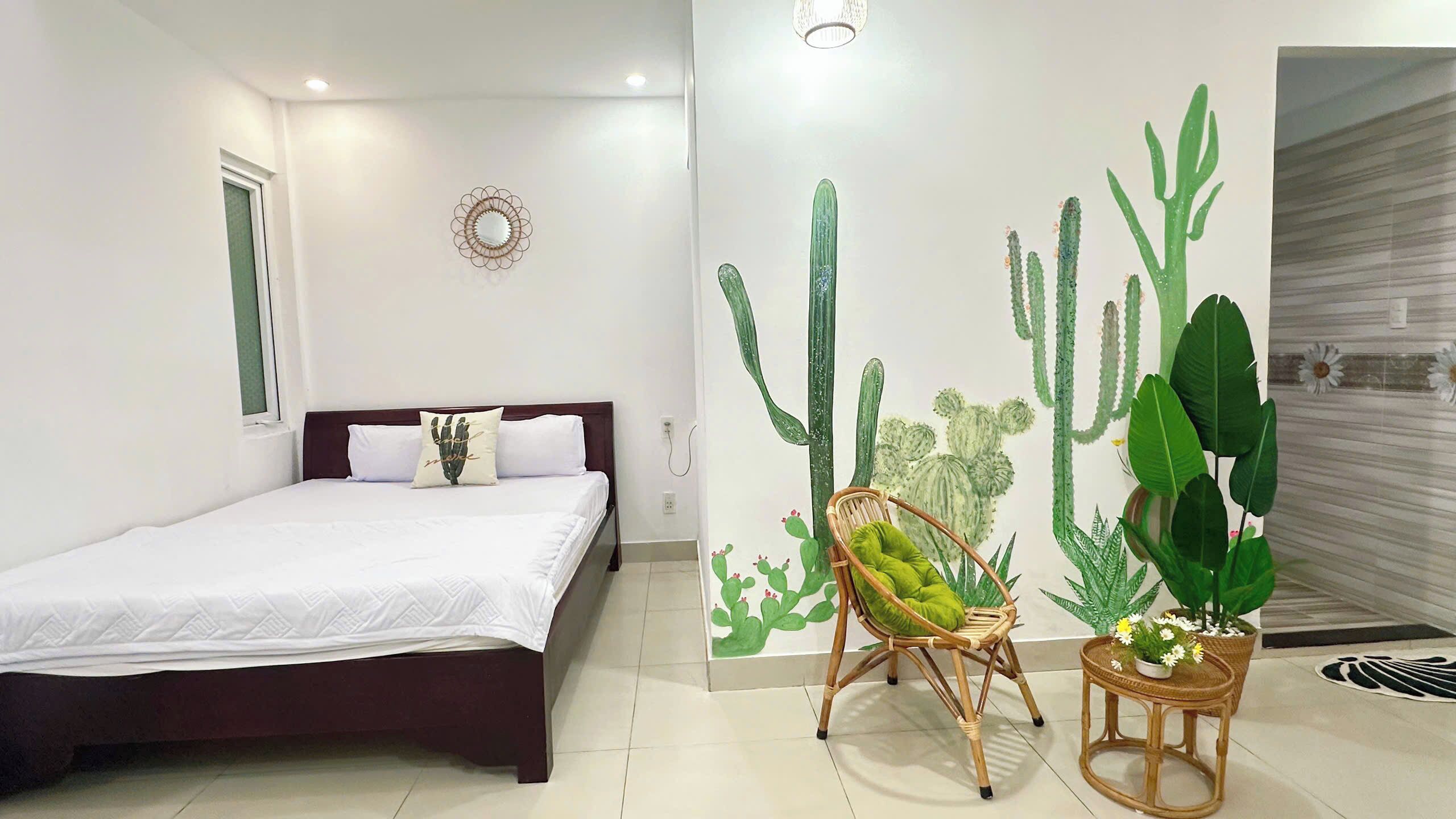A bedroom with a bed, a wall mural of cacti, a wicker chair, and a small table with a potted plant.