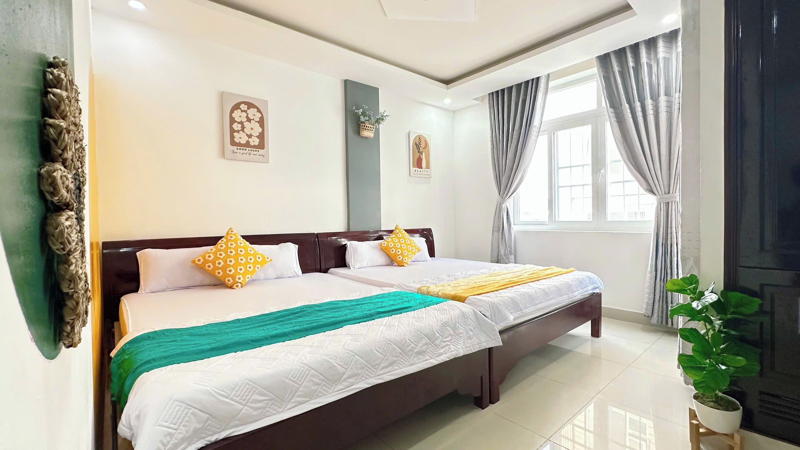 A hotel room with two beds, a large window with curtains, a potted plant, and wall art.