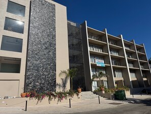 A multi-story building with balconies, a stone facade, and a sign advertising condos for sale. - Elegant 2BR Marina-view condo (Crucecita)