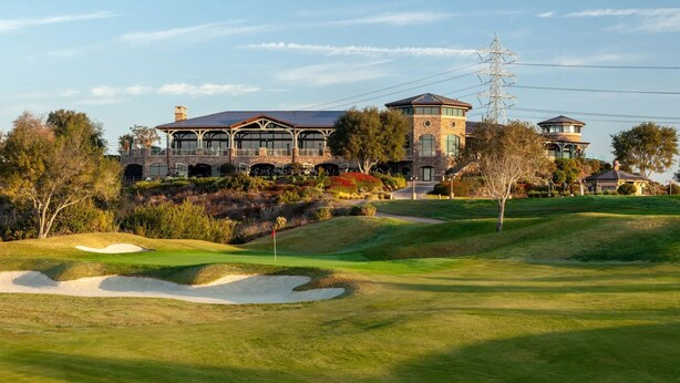 Una casa grande de varios pisos con una torre destacada, rodeada por un campo de golf bien cuidado.