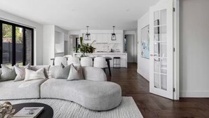 Un soggiorno moderno con un divano modulare grigio, una zona pranzo con isola centrale e una cucina con pensili bianchi e luci a sospensione.