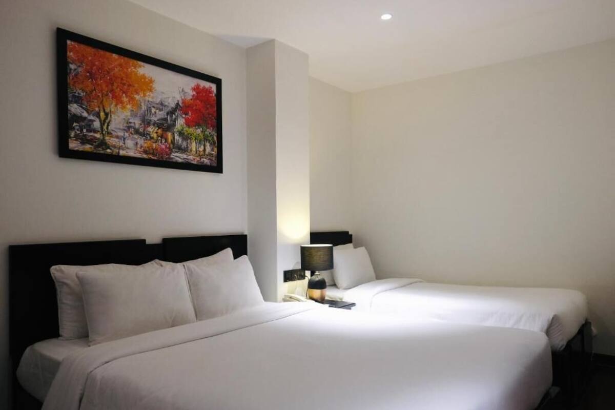 A hotel room with two beds, a painting on the wall, and a nightstand with a lamp.