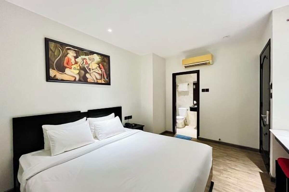 A hotel room with a large bed, a painting on the wall, and an air conditioning unit.