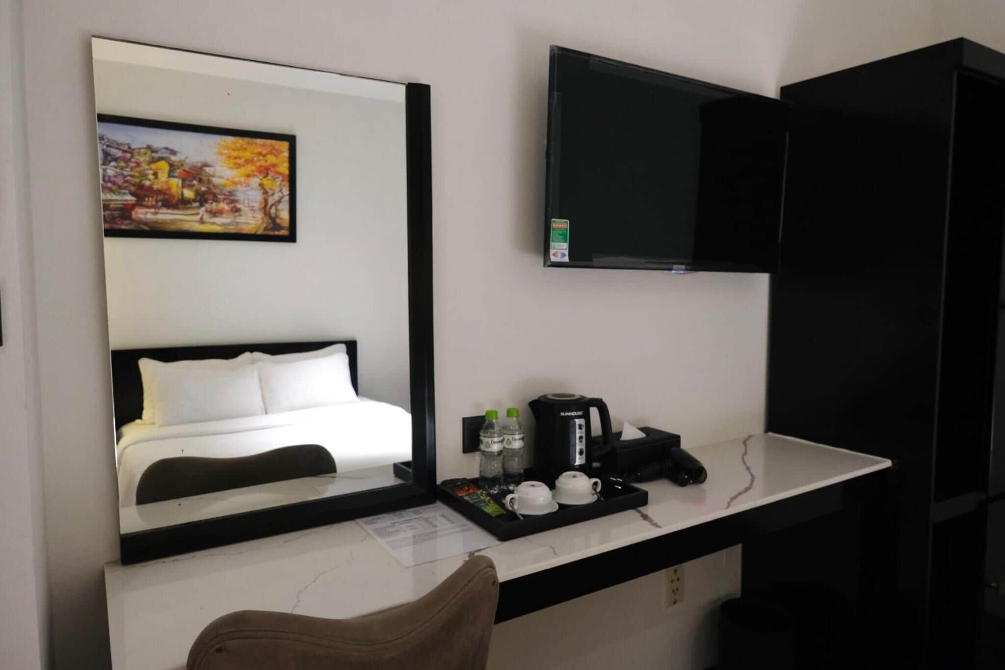 Habitación de hotel con cama, televisión montada en la pared, escritorio con cafetera y bandeja con vasos y botellas de agua.